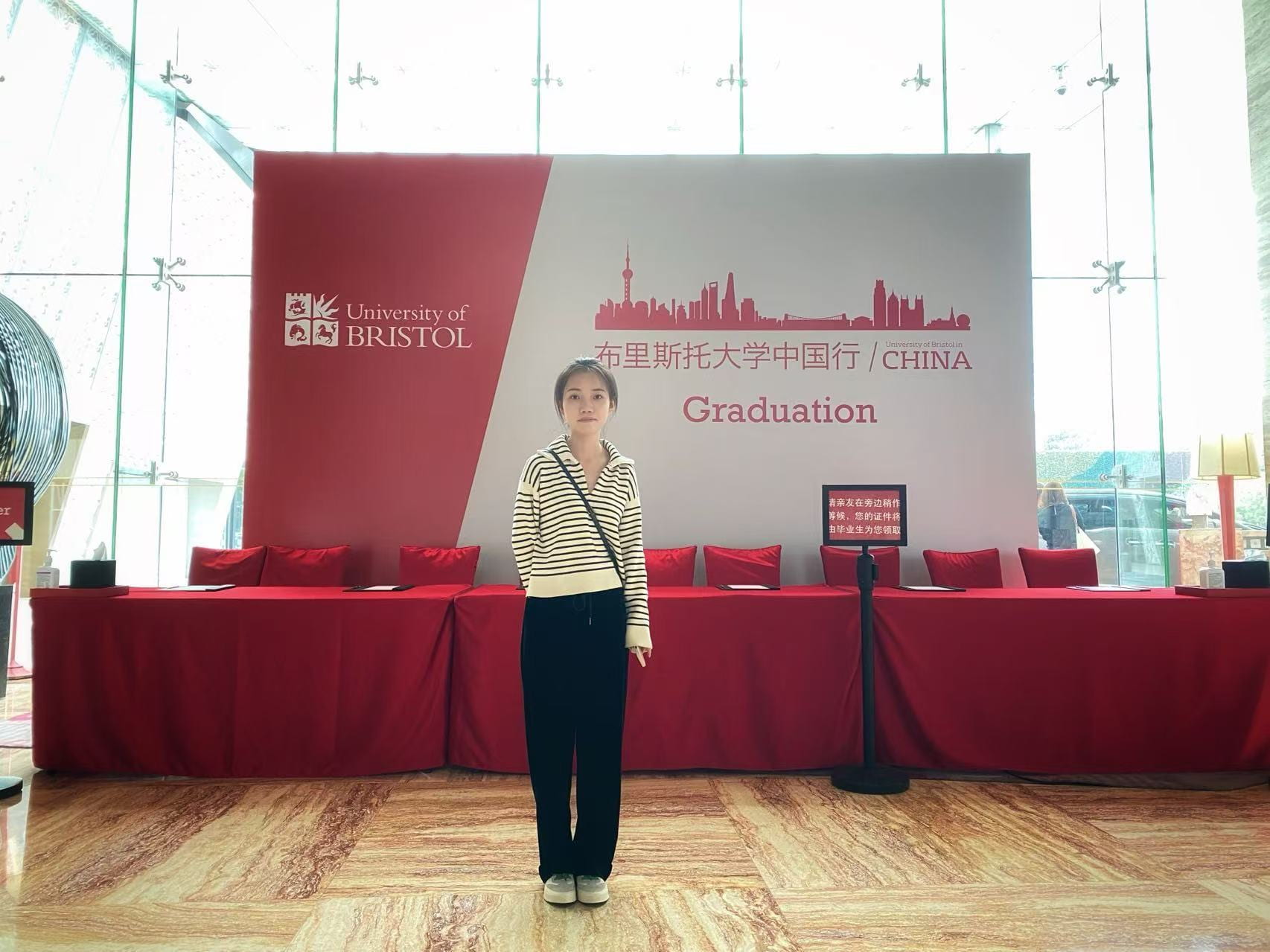 A student standing in front of a University of Bristol banner and three tables covered in red tablecloths